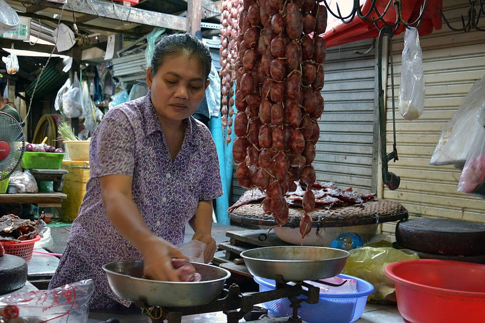 A stallholder in a Cambodian market weighing goods on a hand scale